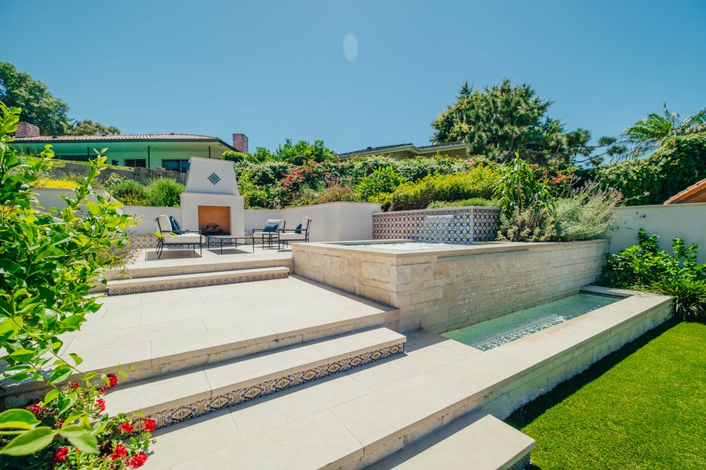Coastal backyard with limestone hardscape, custom spa, fireplace, and tile accents.