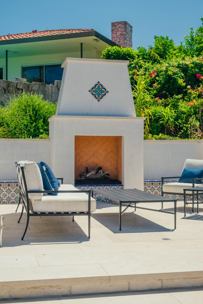 Smooth stucco fireplace with decorative tile and lounge seating in coastal backyard.